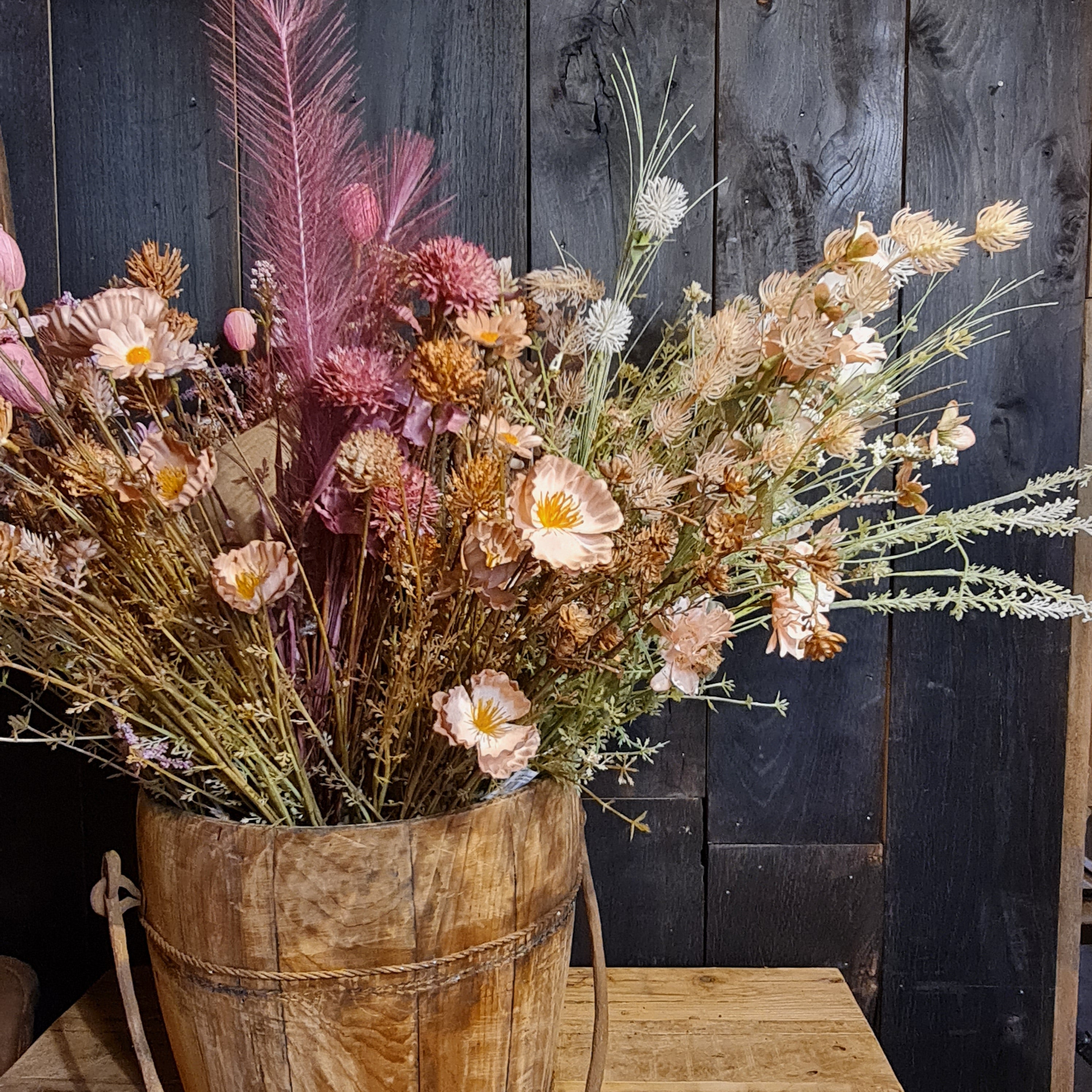 Zijdebloemen in een houten emmer als vaas met landelijke uitstraling